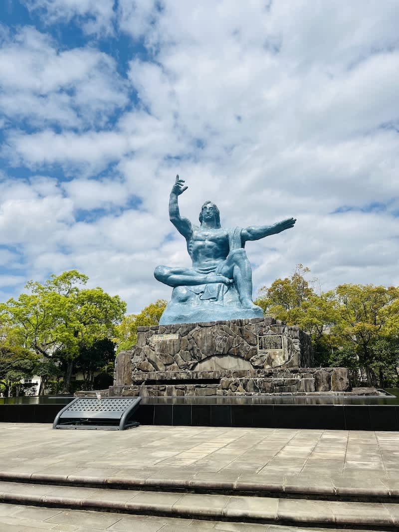 The iconic Peace Statue at Nagasaki Peace Park, with a blue sky backdrop, symbolizing the appeal for peace and remembrance of atomic bomb victims.