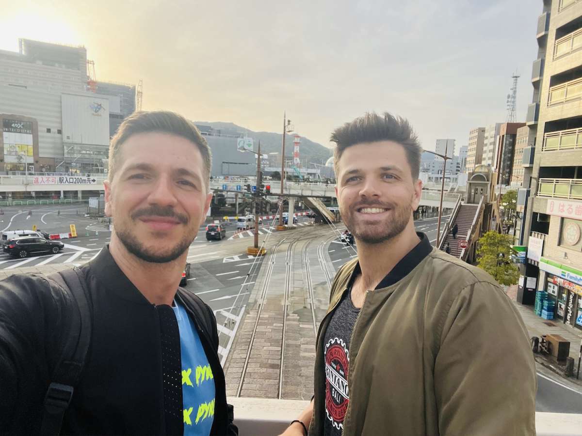 Two smiling men taking a selfie with Nagasaki cityscape in the background, capturing travel memories and the urban vibe of the city.