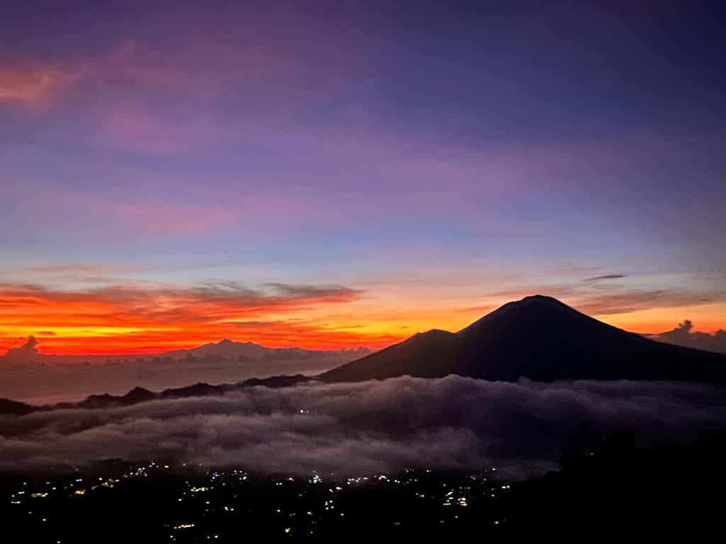 Sunrise view from Mount Batur in Bali, with the sun illuminating the sky in vivid colors and clouds hovering over the volcanic landscape, a magnificent sight for digital nomads.