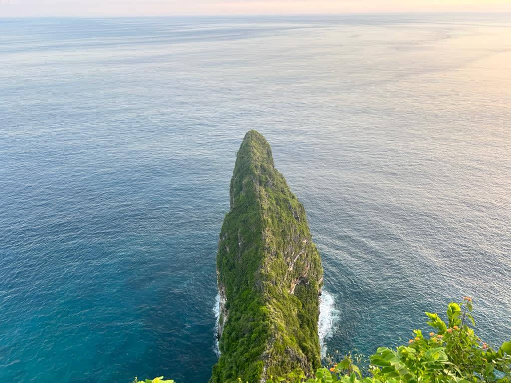 Breathtaking aerial view of a lush green cliff jutting into the azure waters of Nusa Penida, Bali, a favorite remote working spot for digital nomads enjoying Indonesia's natural beauty.