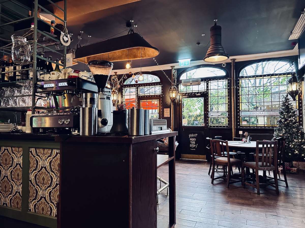 Cozy interior of the Prince Albert pub in Camden, London, with vintage-style decor, a coffee machine on the bar counter, and wooden dining tables set in a warm, inviting atmosphere.