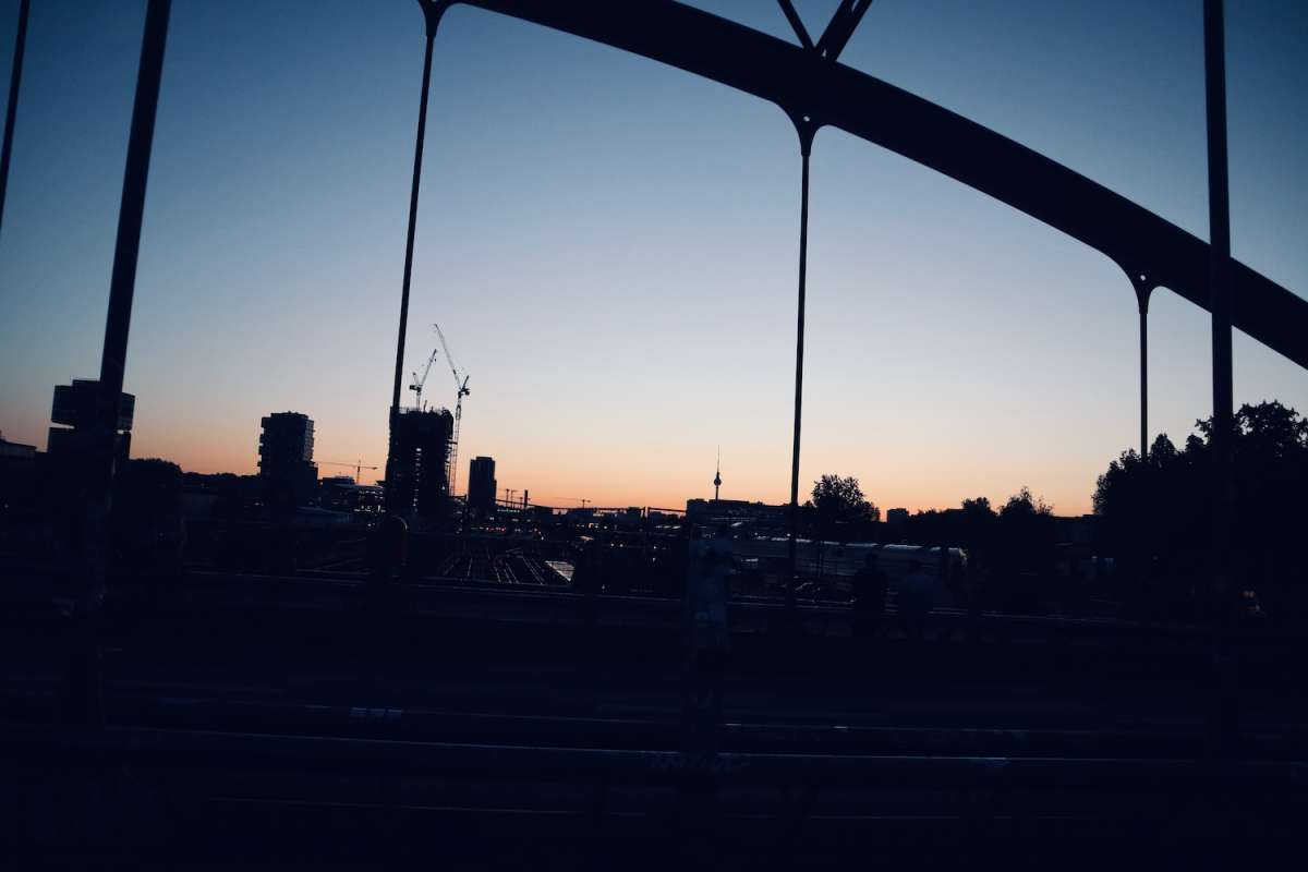 Twilight view from a bridge in Berlin, featuring urban outlines and construction cranes against a sunset backdrop, capturing the city’s ongoing development.