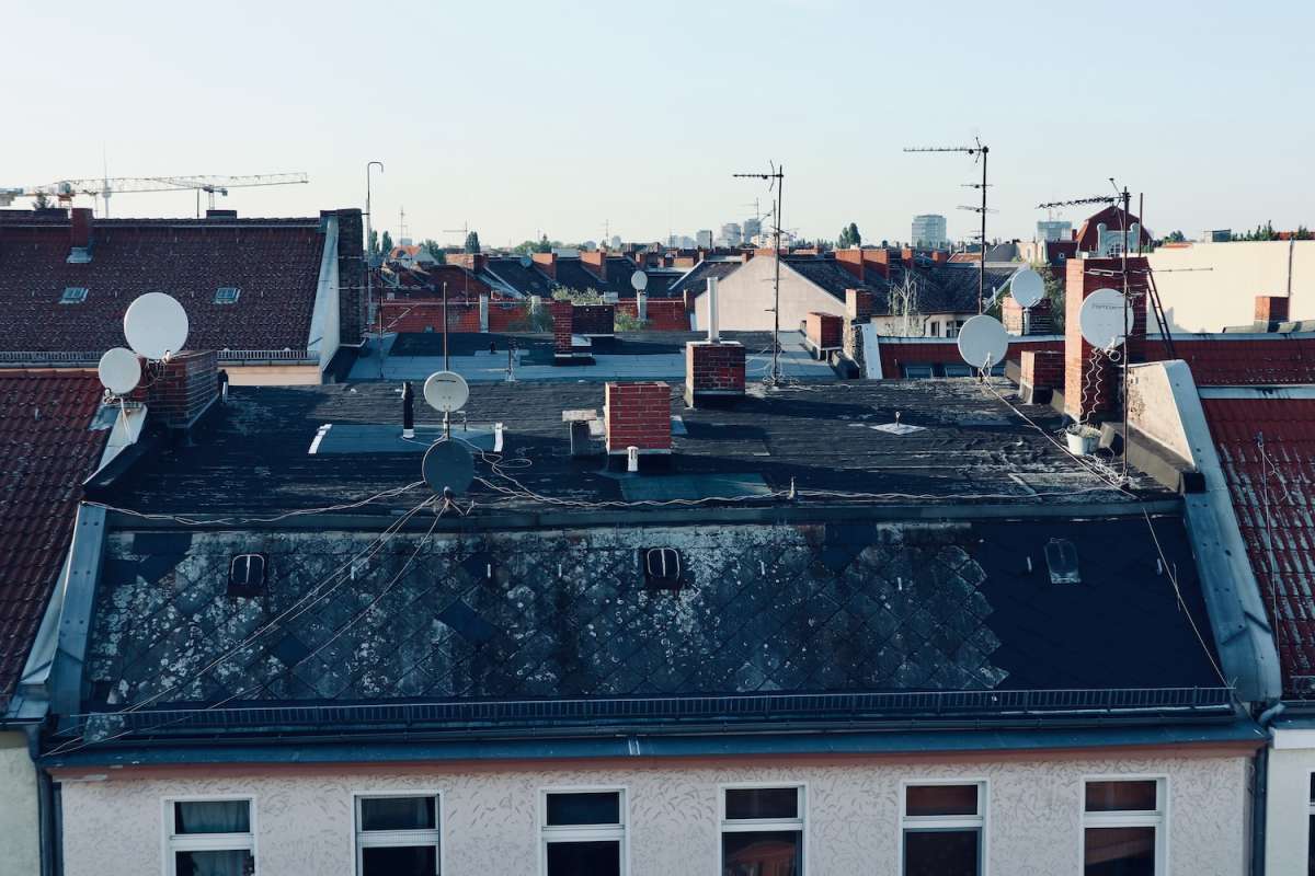 Diverse rooftops with multiple satellite dishes and antennas during daytime in Berlin, showcasing the city's alternative urban texture.