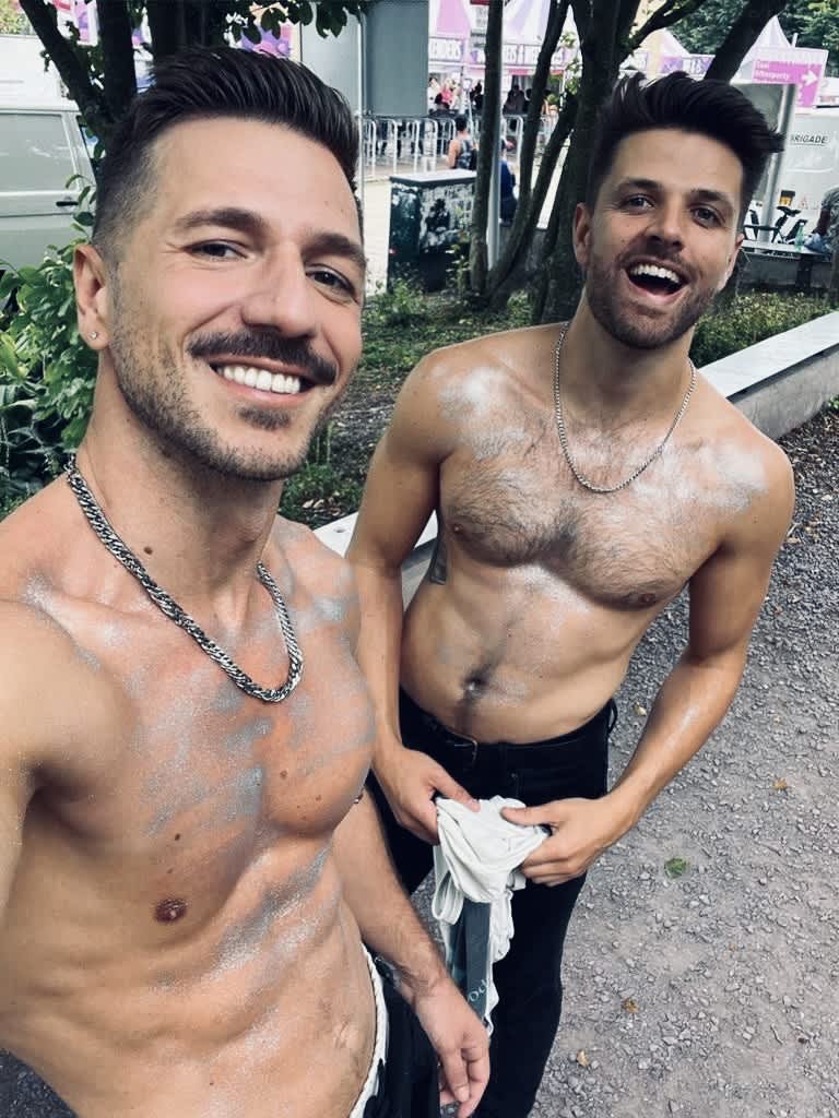 Two shirtless men covered in glitter smiling for the camera at the Milkshake Festival Amsterdam, capturing a moment of fun and camaraderie among festival attendees.