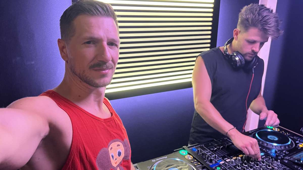 Two men DJing at PIRATE studios DJ booth in Prenzlauer Berg, Berlin, with colorful lighting and a vibrant crowd, embodying the alternative nightlife scene in Berlin.