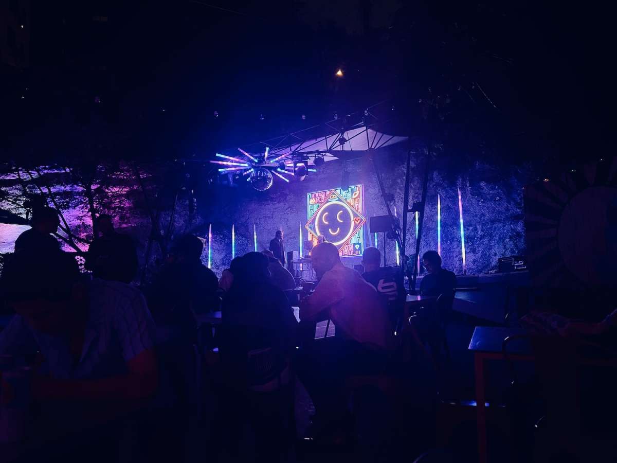 Nighttime view of a vibrant live music event at Cheer Up Charlies, a popular gay bar in Austin, Texas, with purple and blue lighting and a crowd enjoying the performance.