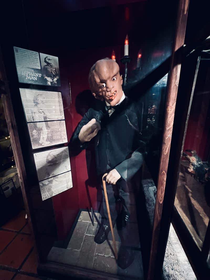 Exhibit of a life-sized figure of the Elephant Man in a dark, candle-lit room at the Museum of Weird in Austin, Texas, with historical information displayed beside him.