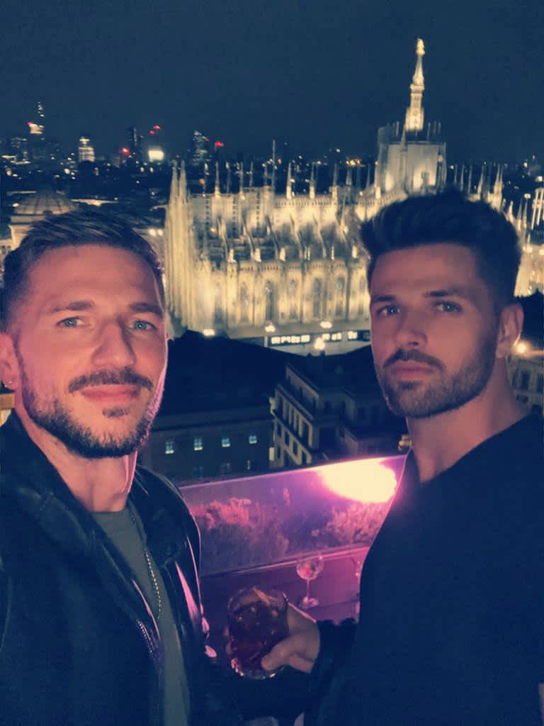 Two men enjoying aperitivo on the Terrazza Martini in Milan, with a stunning view of the illuminated Duomo in the background, showcasing a chic and memorable evening.