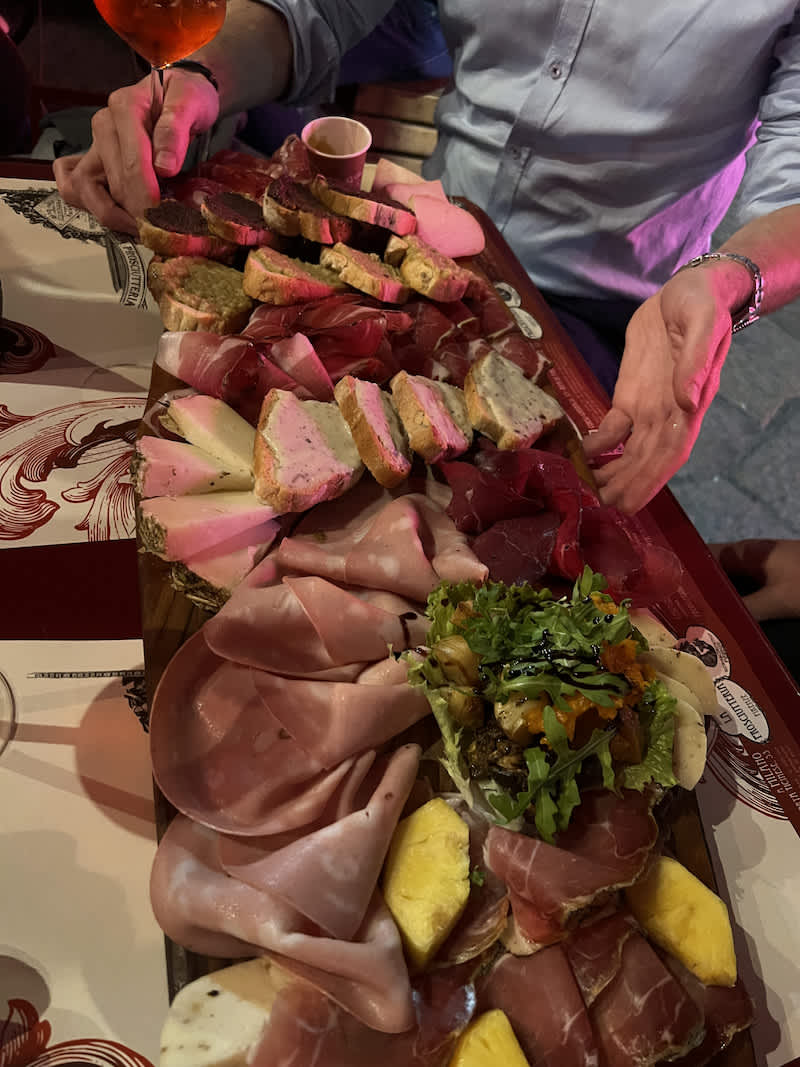 A lavish charcuterie board filled with various types of cured meats, cheeses, and bread, served on a rustic wooden board at a cozy Milanese eatery, perfect for an aperitivo.