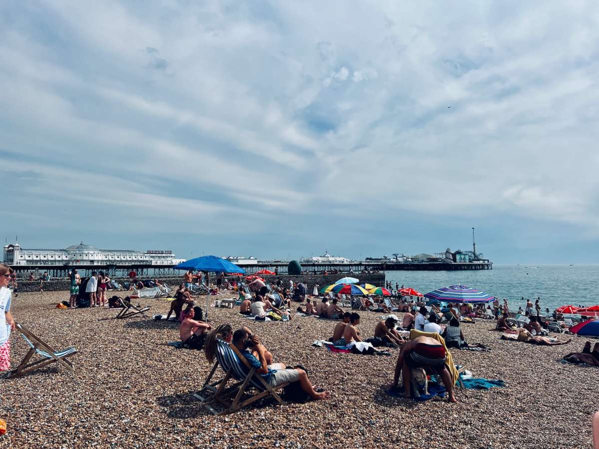 Vibrant scene at Brighton beach with a crowd enjoying the sunny weather, colorful umbrellas, and the Brighton Pier in the background, a lively part of gay Brighton.