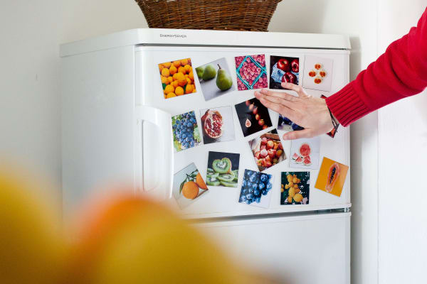 A fridge freezer covered in fridge magnets. A womans hand is closing the freezer door.