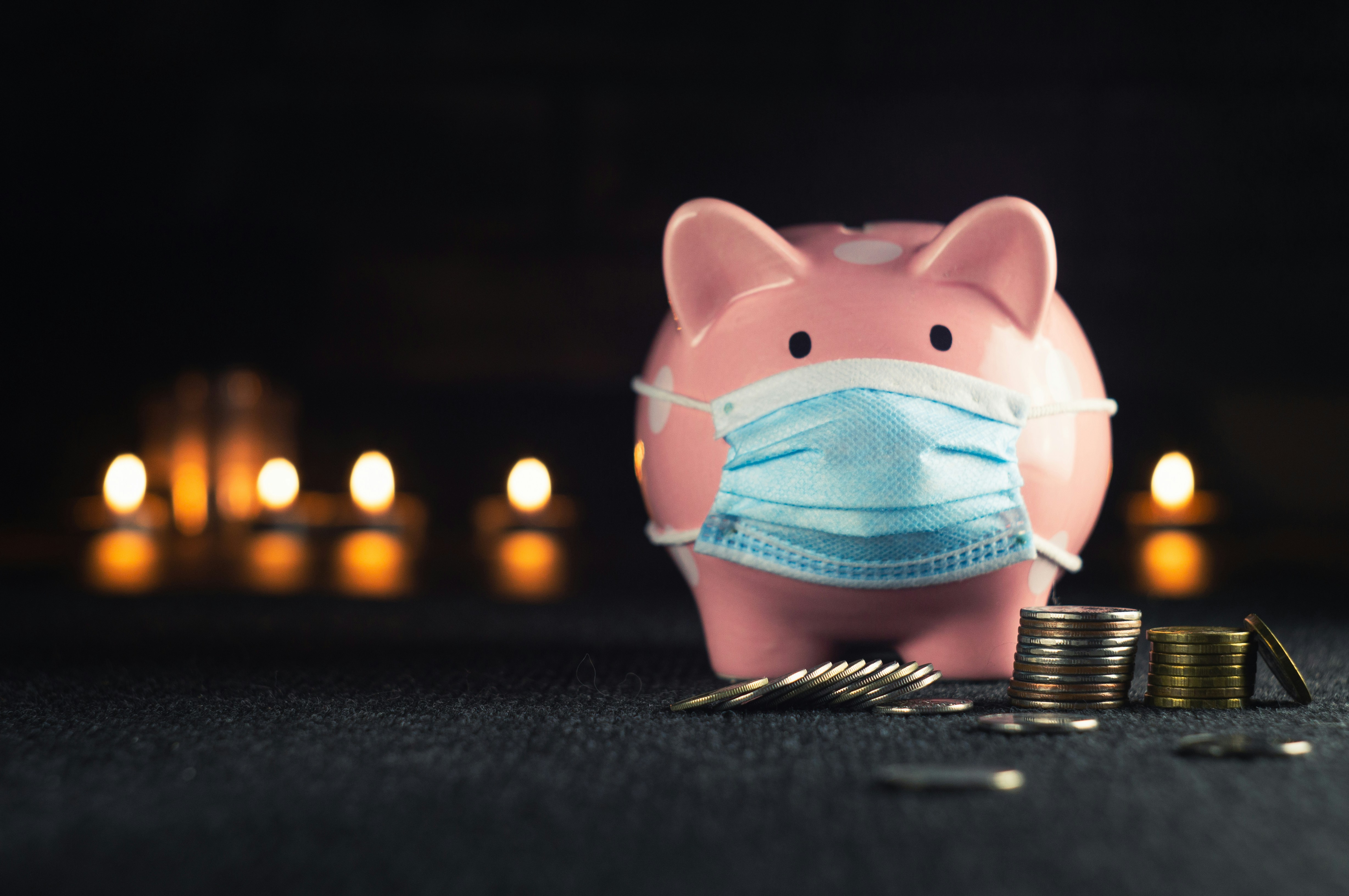 a traditional pig money bank wearing a surgical mask, stood in front of a pile of coins