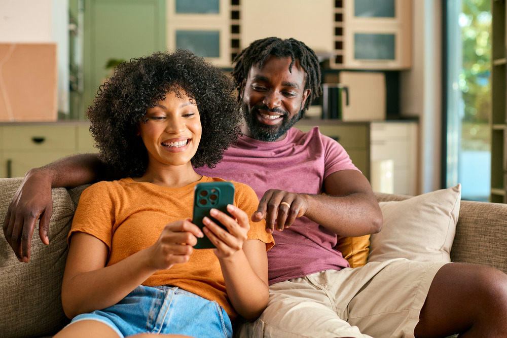 A couple sat on the sofa happily looking at a smartphone