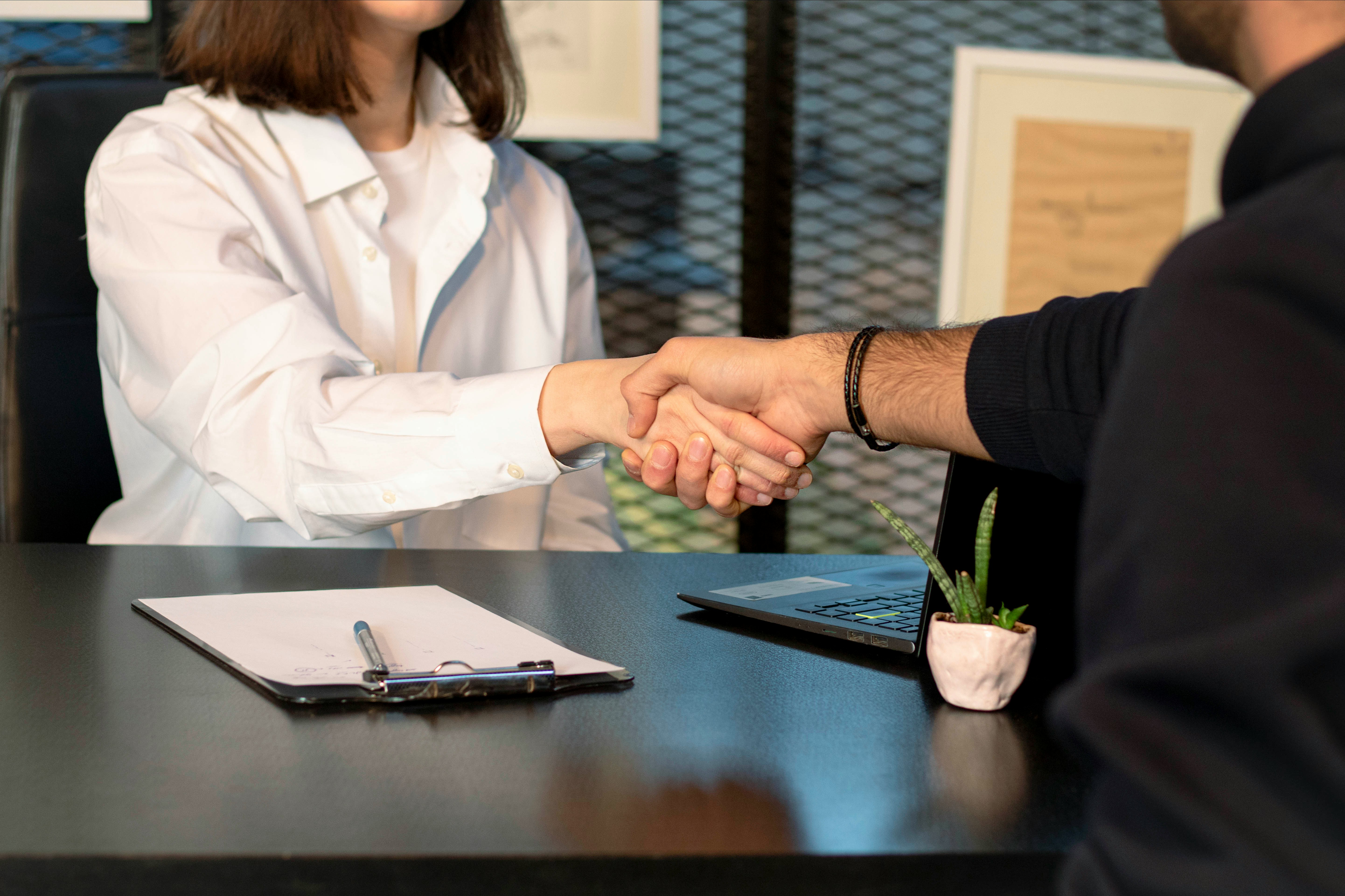 a man and woman shaking hands over a pile of paperwork on a desk