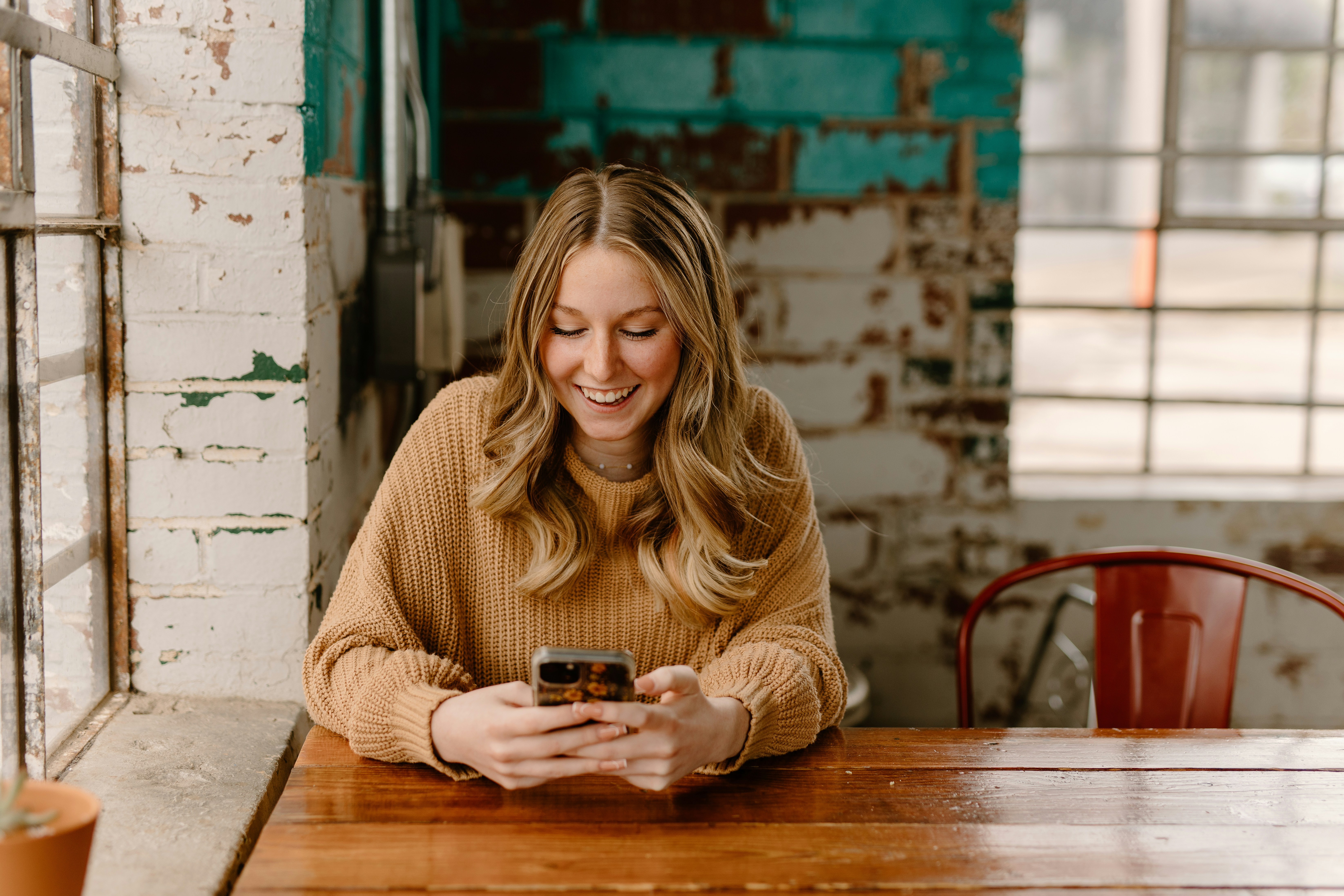 a lady sat at a desk, looking at her mobile phone and smiling