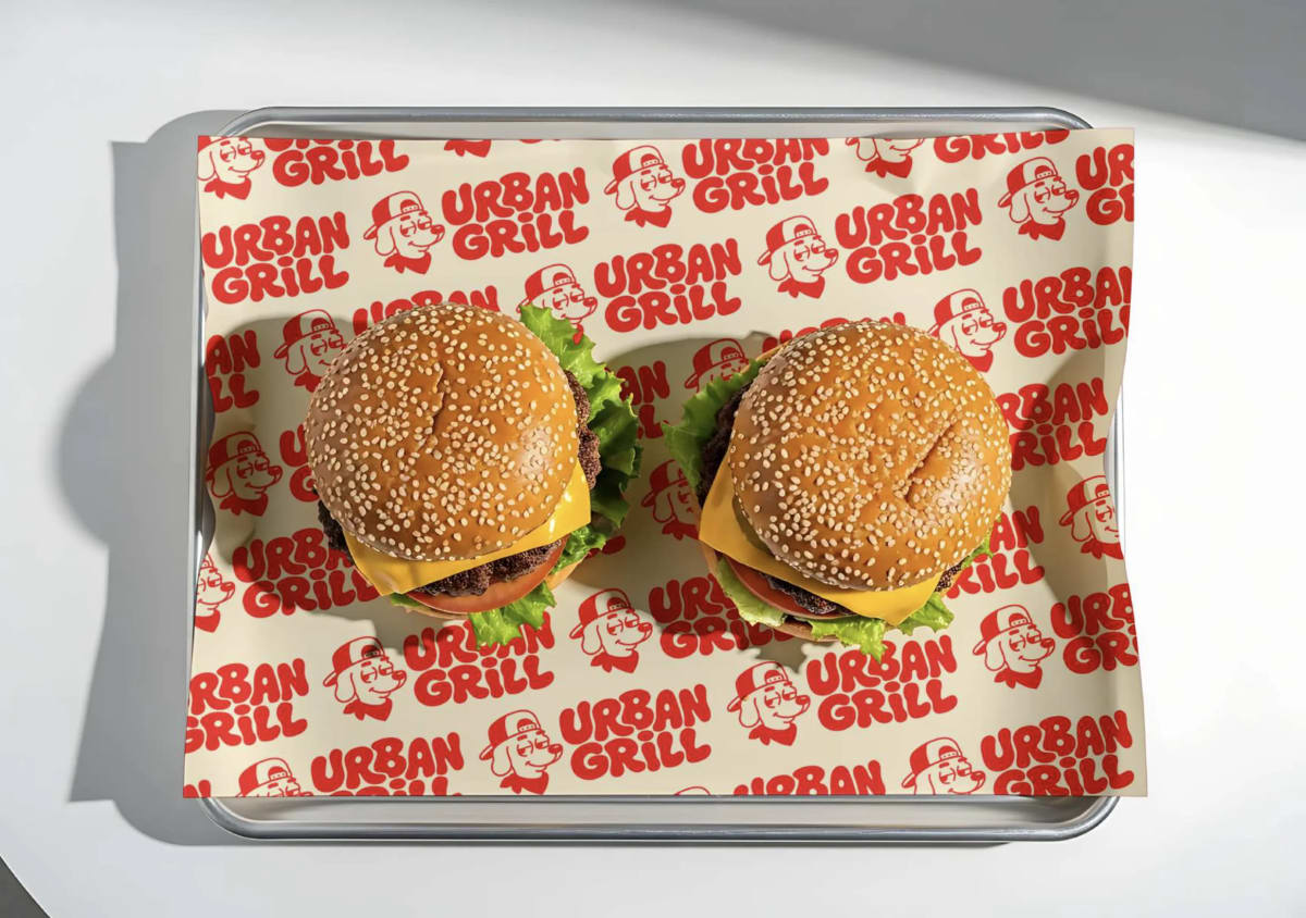 Dos hamburguesas sobre el papel estampado de Urban Grill en una bandeja metálica, de Andrea Jurado, alumna de Diseño Gráfico y Motion Graphics en TRAZOS