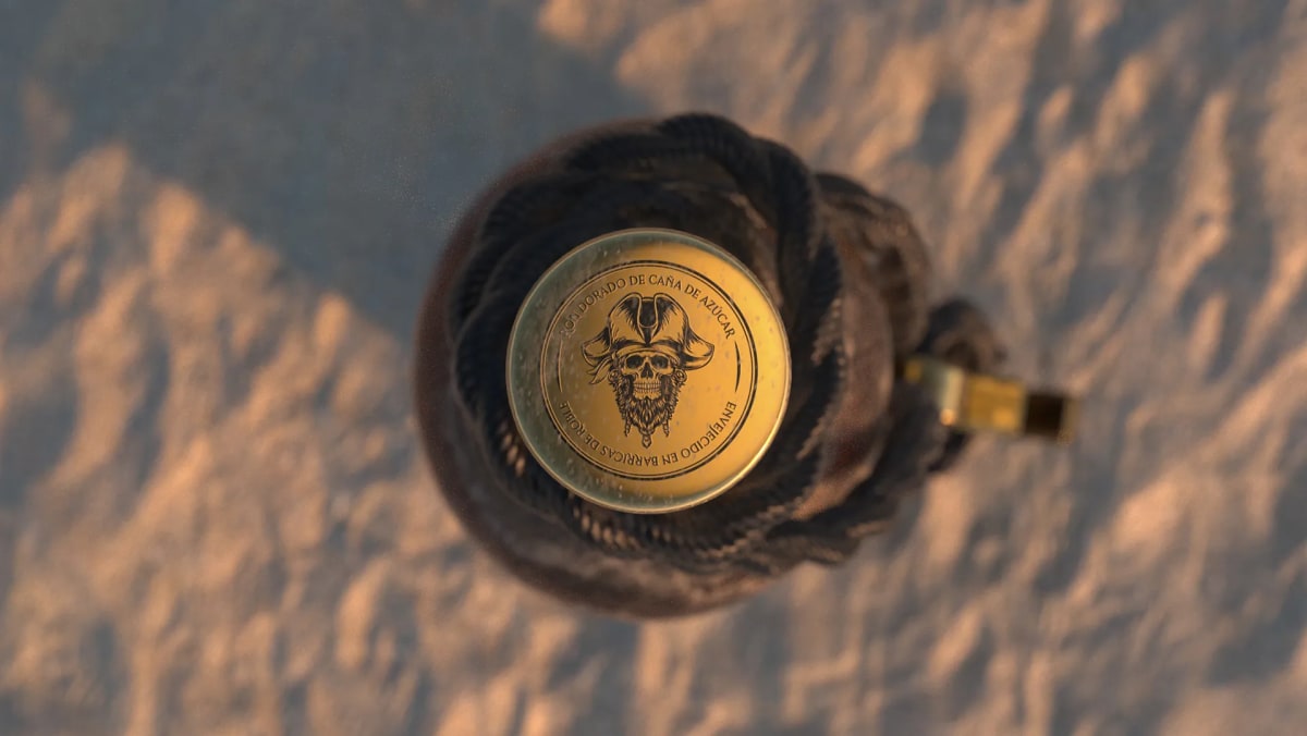 Vista cenital del tapón dorado del ron pirata Barbanegra con medallón de calavera sobre la arena, de Ánder Sánchez, alumno de Diseño Gráfico y Motion Graphics en TRAZOS