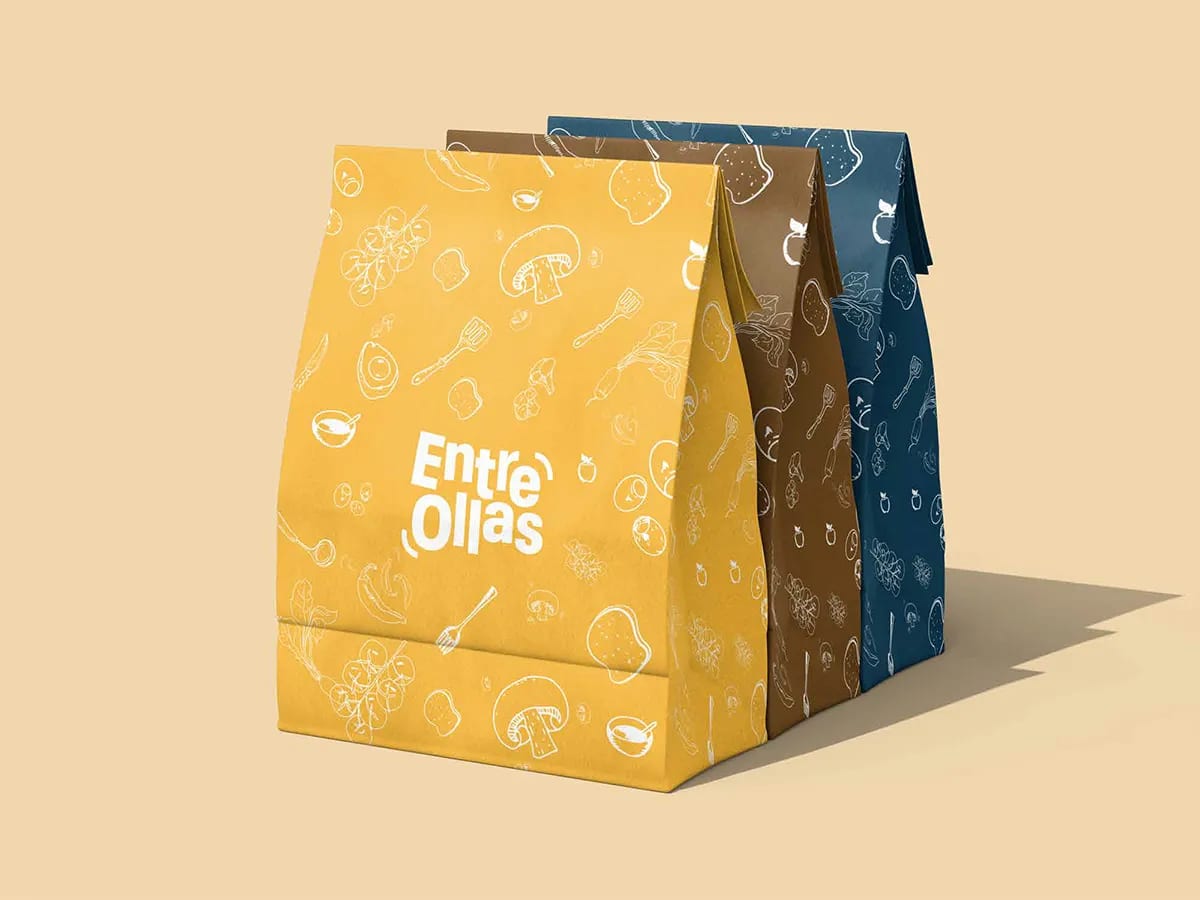 Bolsas de papel para llevar de la marca Entre Ollas en amarillo, marrón y azul con patrón de alimentos, de Marina Gabilondo Calleja, alumna de Diseño Gráfico y Motion Graphics en TRAZOS