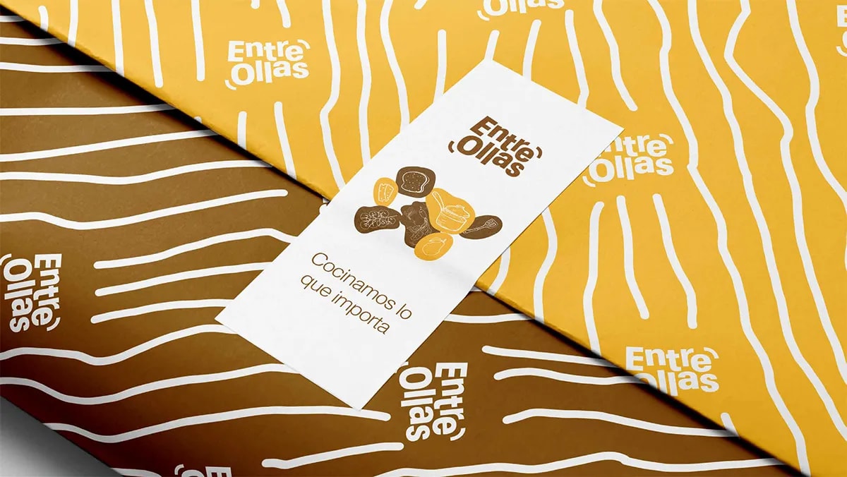 Papel de regalo con patrón de ondas y logotipo de la marca Entre Ollas junto a una tarjeta, de Marina Gabilondo Calleja, alumna de Diseño Gráfico y Motion Graphics en TRAZOS