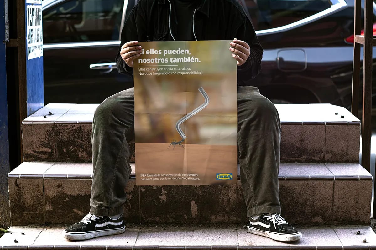 Persona sentada sosteniendo un cartel de IKEA Sostenible con una hormiga, de Maren Alberdi Hernández, alumna de Diseño Gráfico y Motion Graphics en TRAZOS