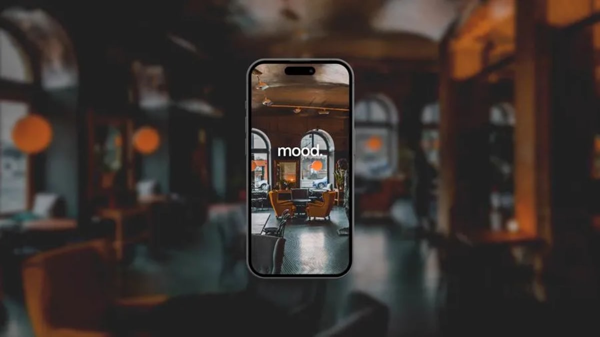 Mockup en móvil de la pantalla de inicio de la app mood sobre un interior tipo cafetería desenfocado, de Miriam Paredes del Río, alumna de UX/UI/Web en TRAZOS