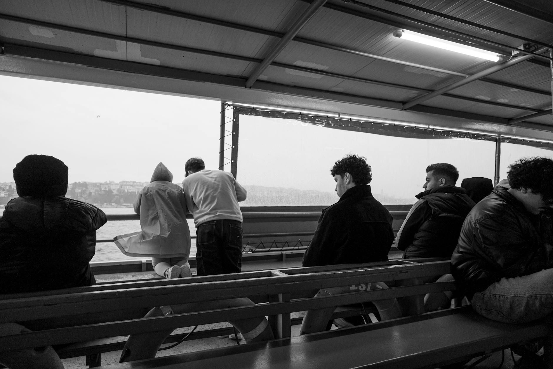 Adults on a ferry in Istanbul, capturing candid city views in black and white.