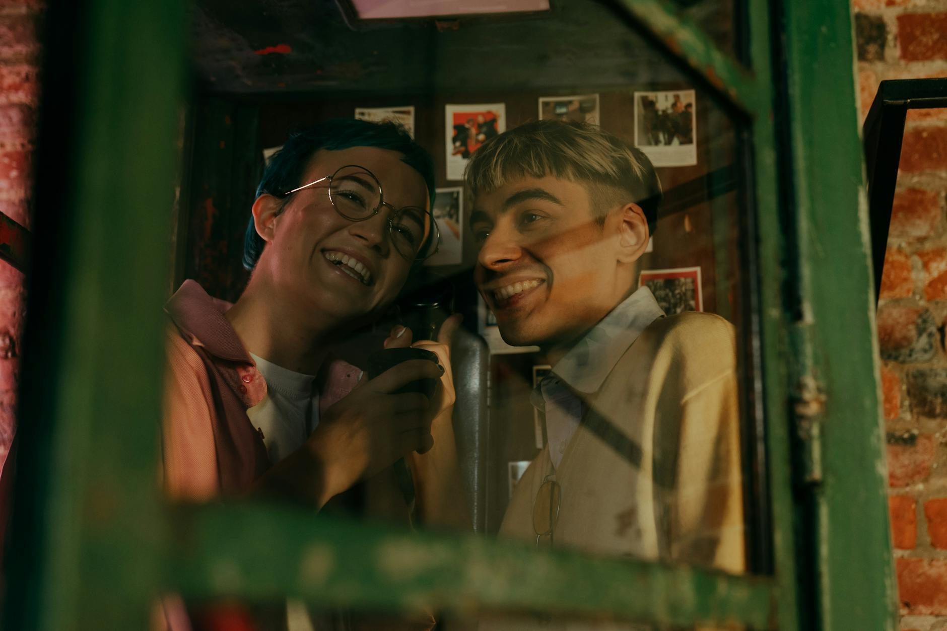 Teenagers smiling and talking in a vintage phone booth with a retro vibe.