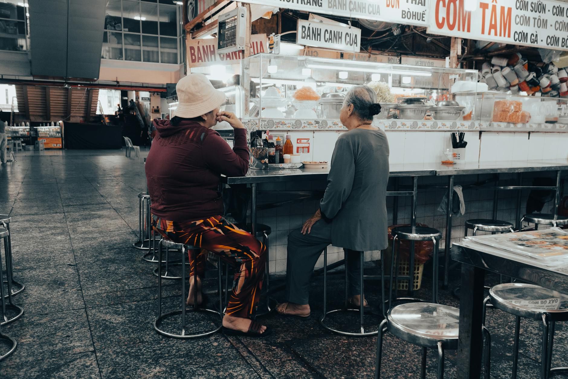 Two individuals enjoy a meal at a casual Vietnamese market stall in Ho Chi Minh City.