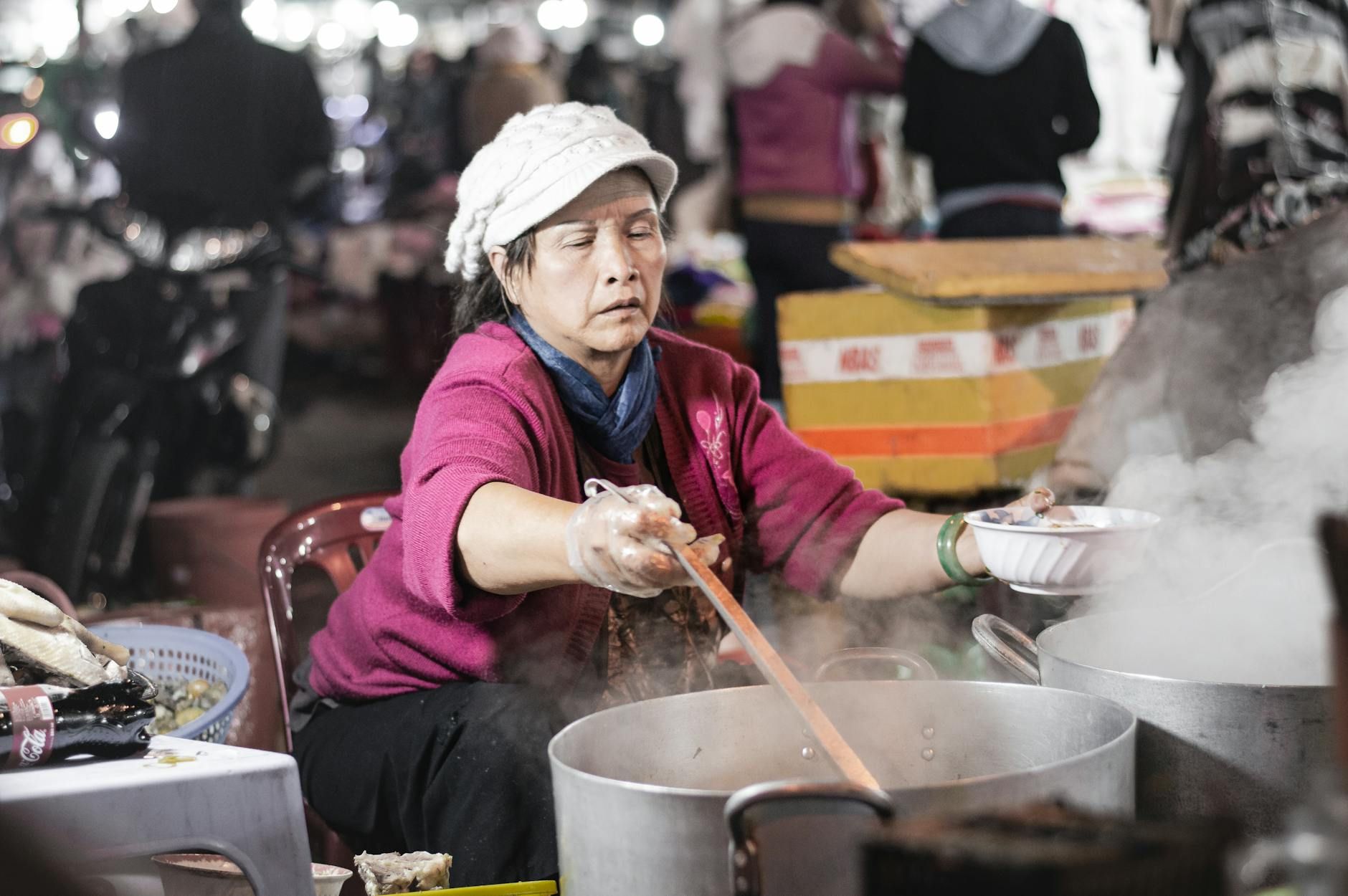 Elderly woman cooking traditional Vietnamese dish in Đà Lạt night market, Việt Nam.