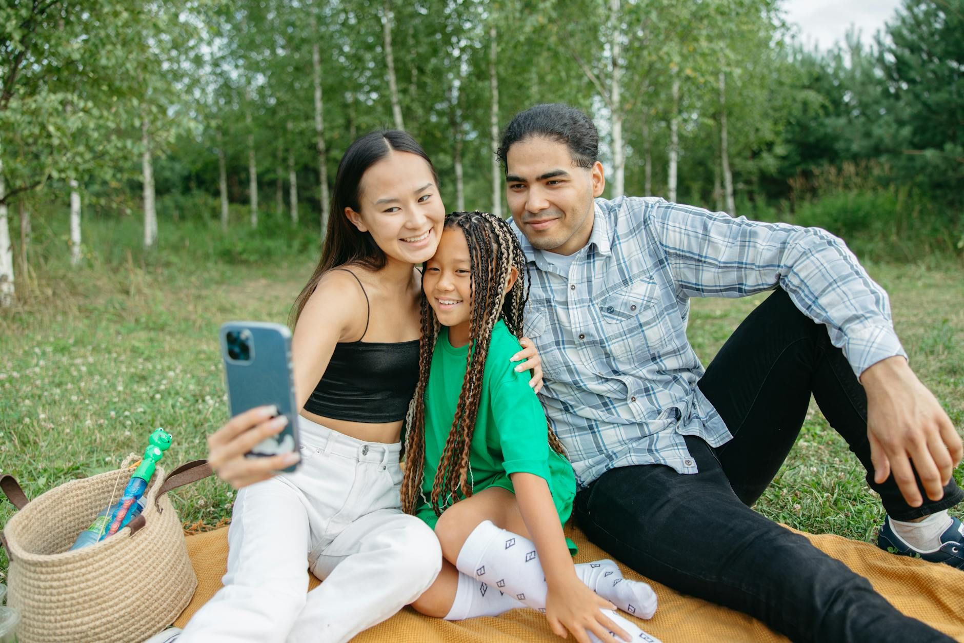 A joyful family enjoying a picnic and taking selfies in a sunny park setting.
