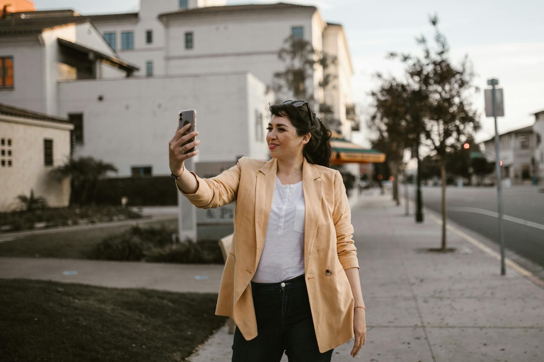 Confident woman in a blazer takes a selfie outdoors, capturing a modern city vibe.