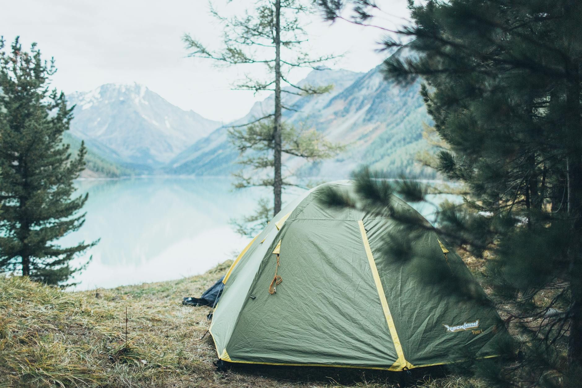 A peaceful campsite by a lake with a tent and scenic mountain backdrop.