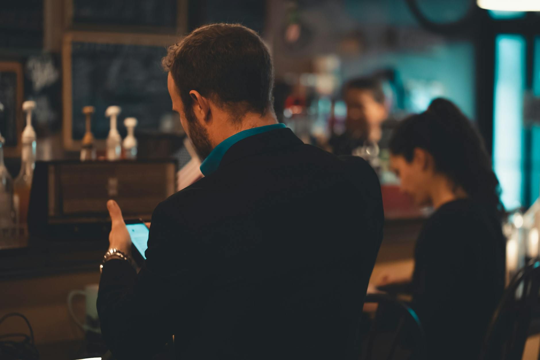 Adult man in a suit using a smartphone inside a cozy coffee shop setting.
