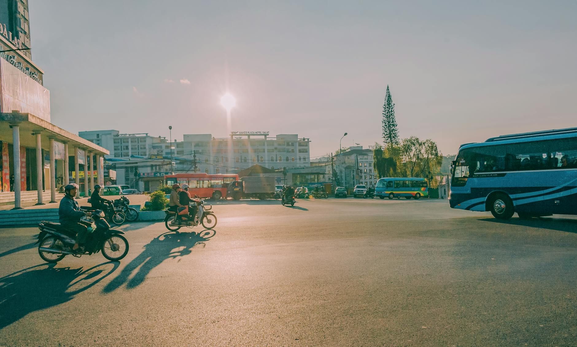 Urban street scene with motorcycles and buses during sunset, showcasing vibrant city life.