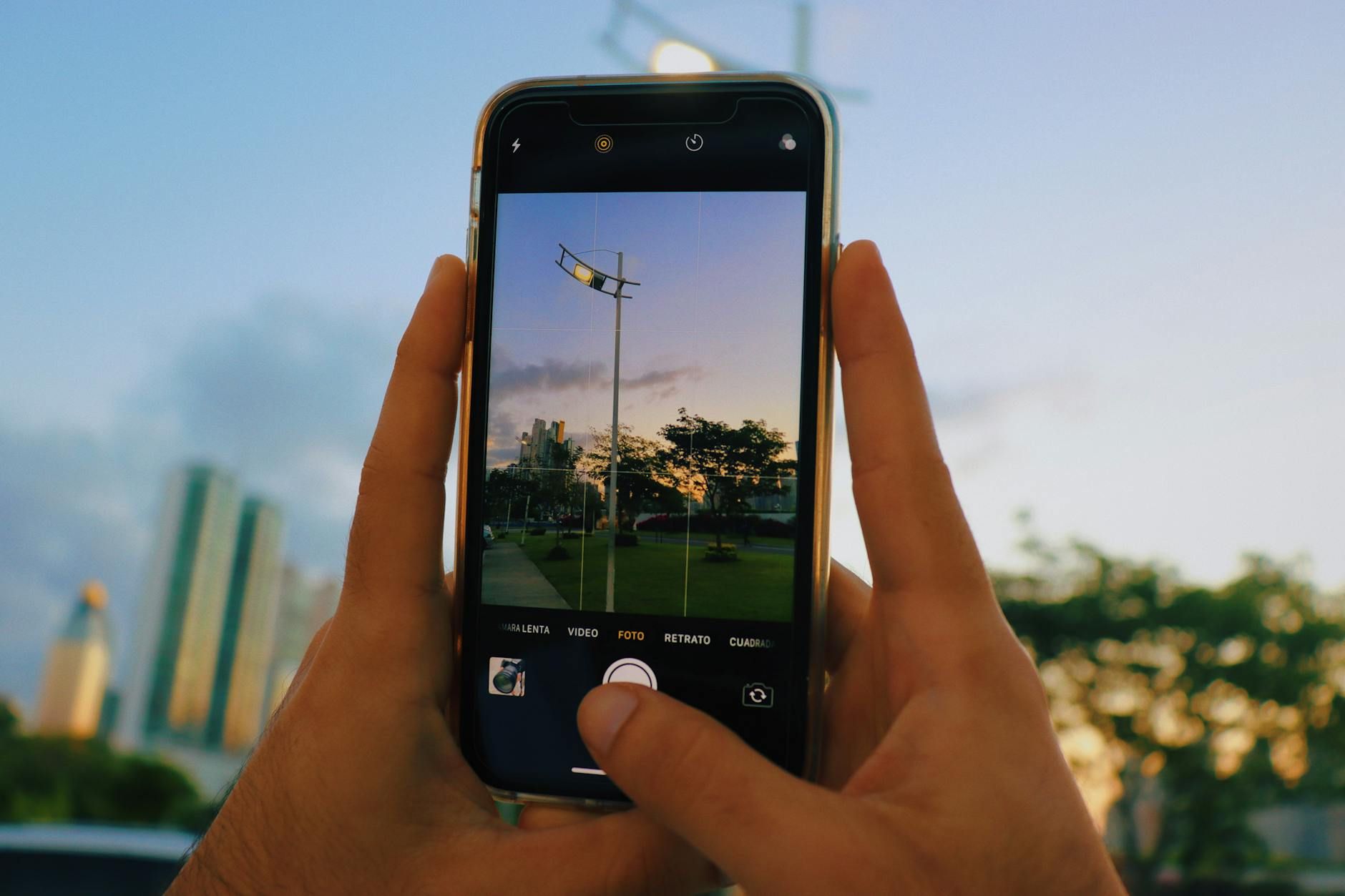 A close-up shot of a smartphone taking a photo of a city skyline during sunset.