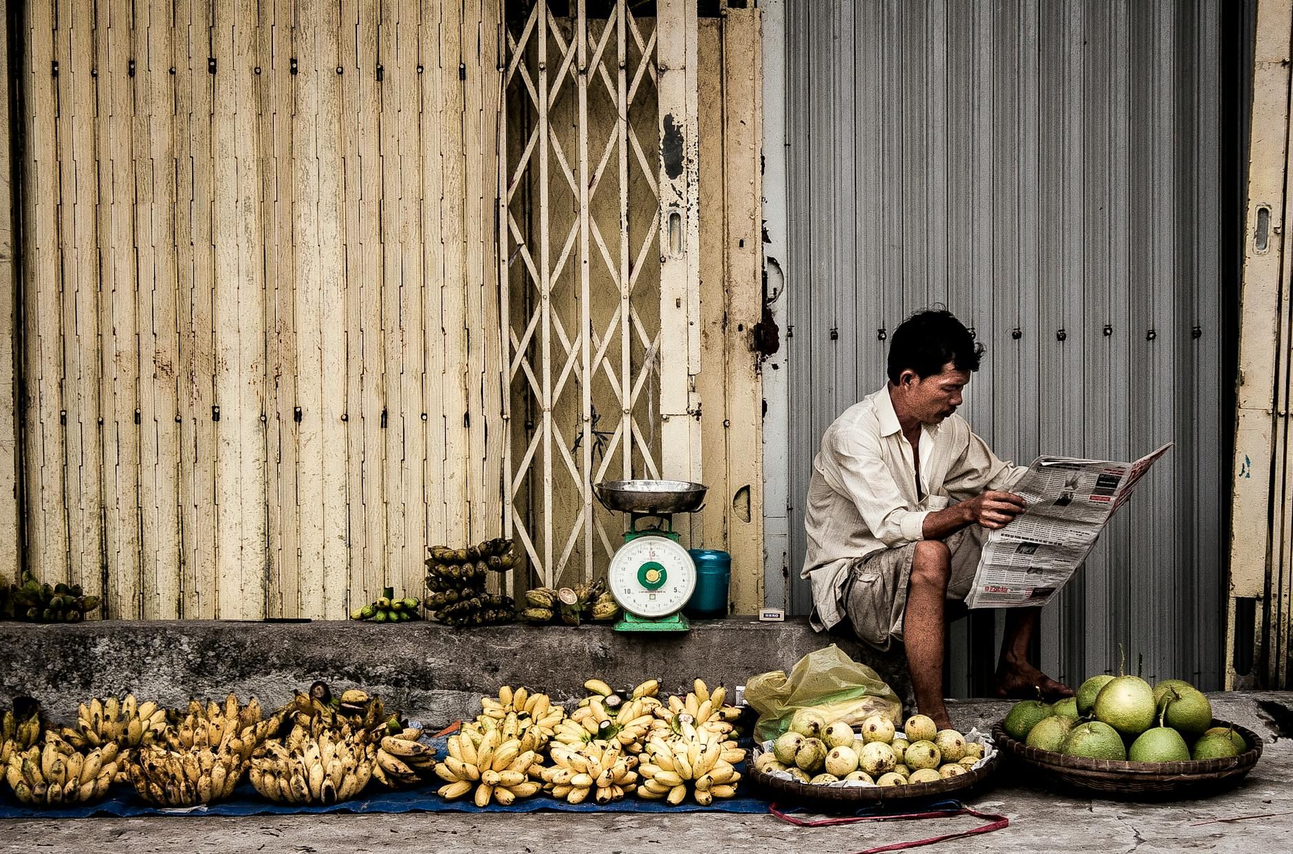 A Vietnamese vendor reads a newspaper beside fresh fruits on a street market in Ho Chi Minh City.