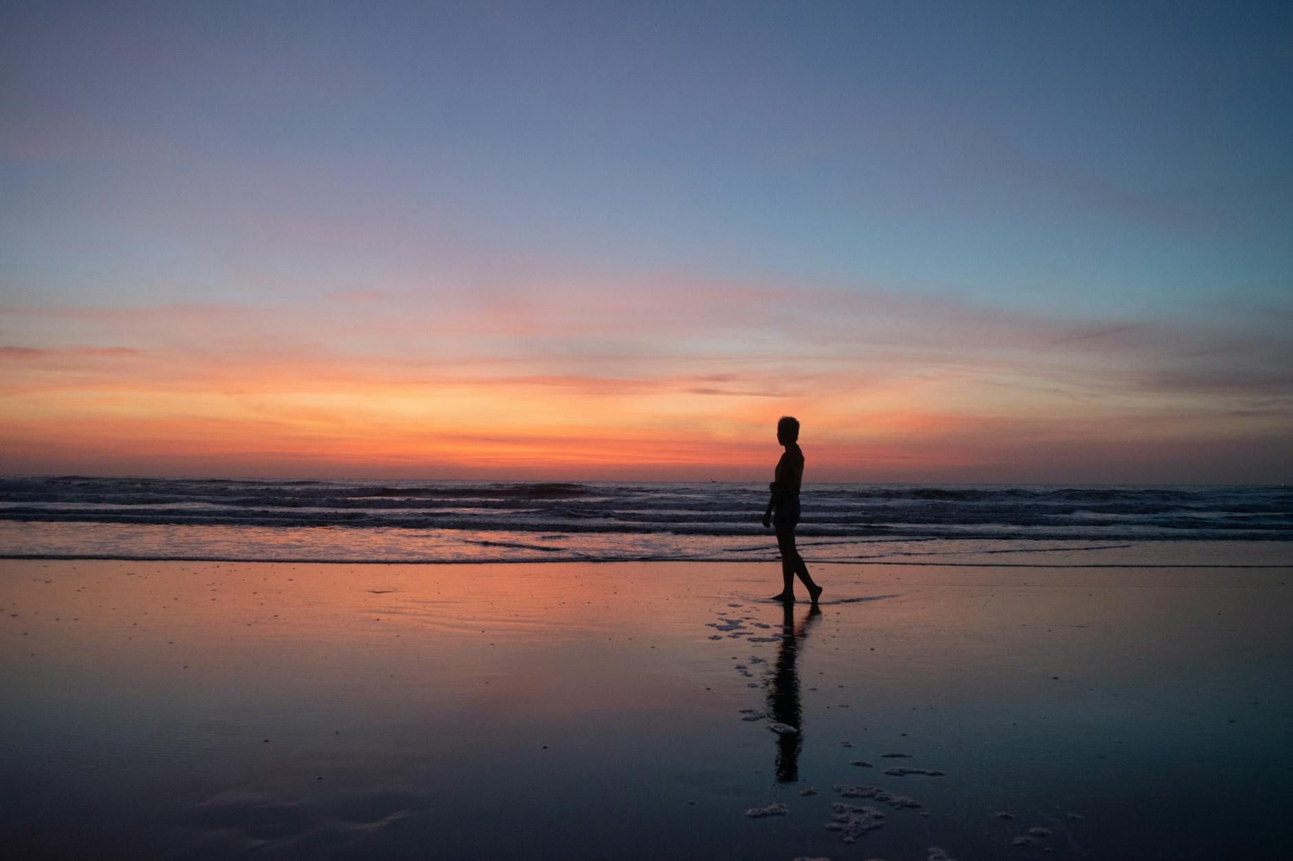 A lone silhouette walks on Vũng Tàu beach at sunset, reflecting serene beauty.