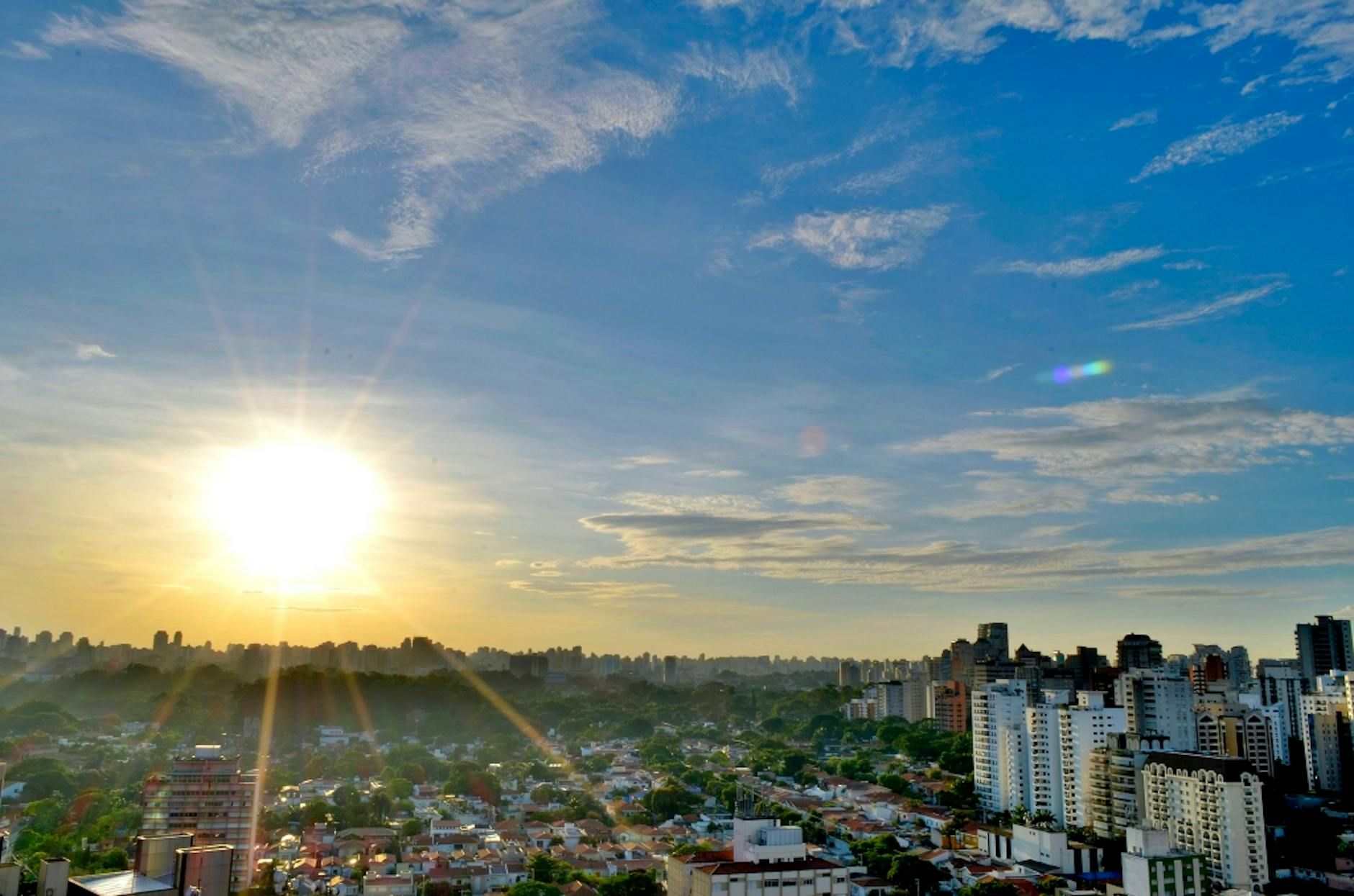 Capture of a vibrant cityscape with sun glare and a clear blue sky, showcasing modern urban architecture.