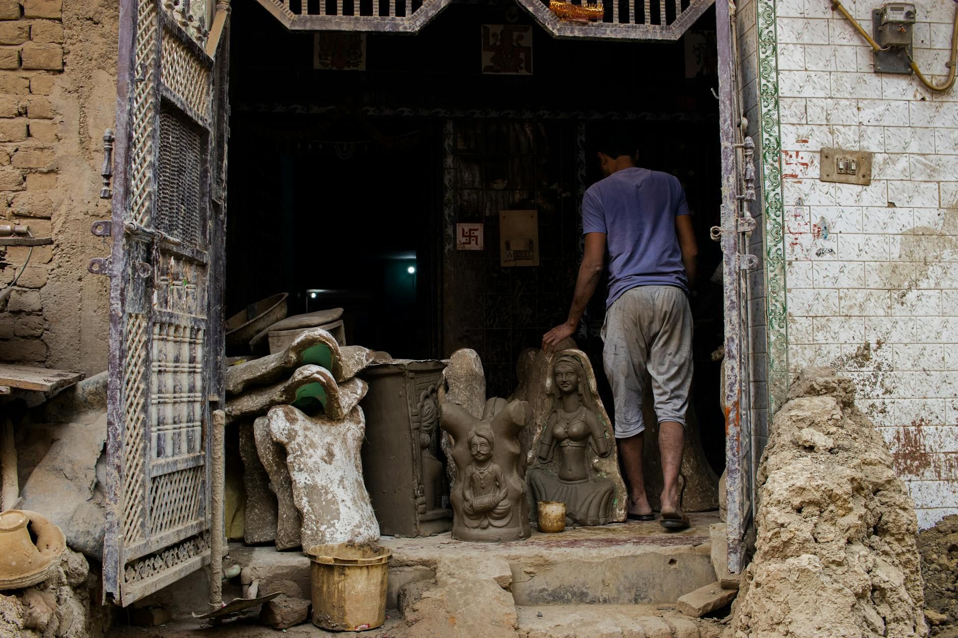 A man among clay sculptures at a traditional Indian pottery workshop.