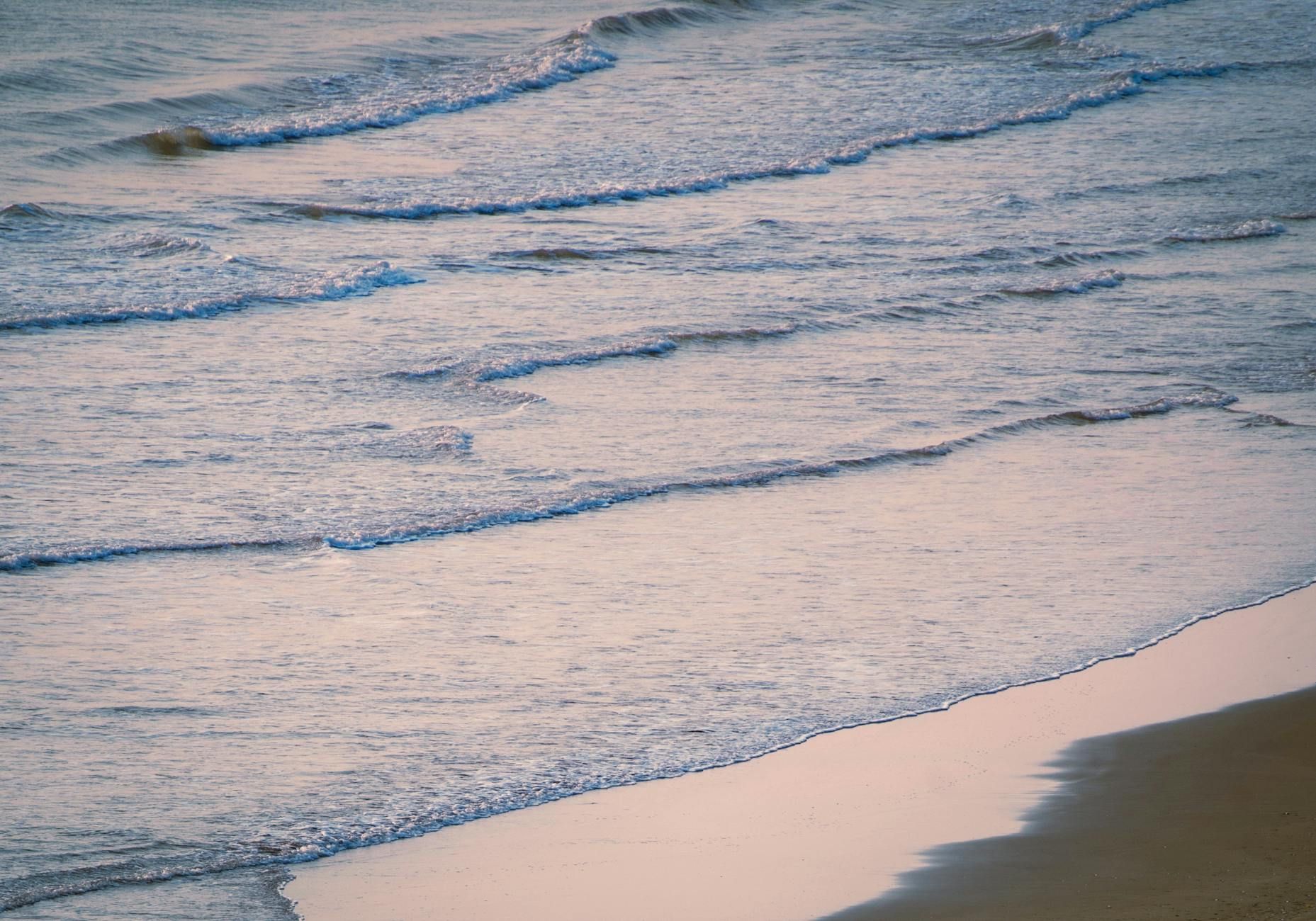A peaceful view of gently rolling waves hitting the sandy beach at dawn, capturing tranquility.