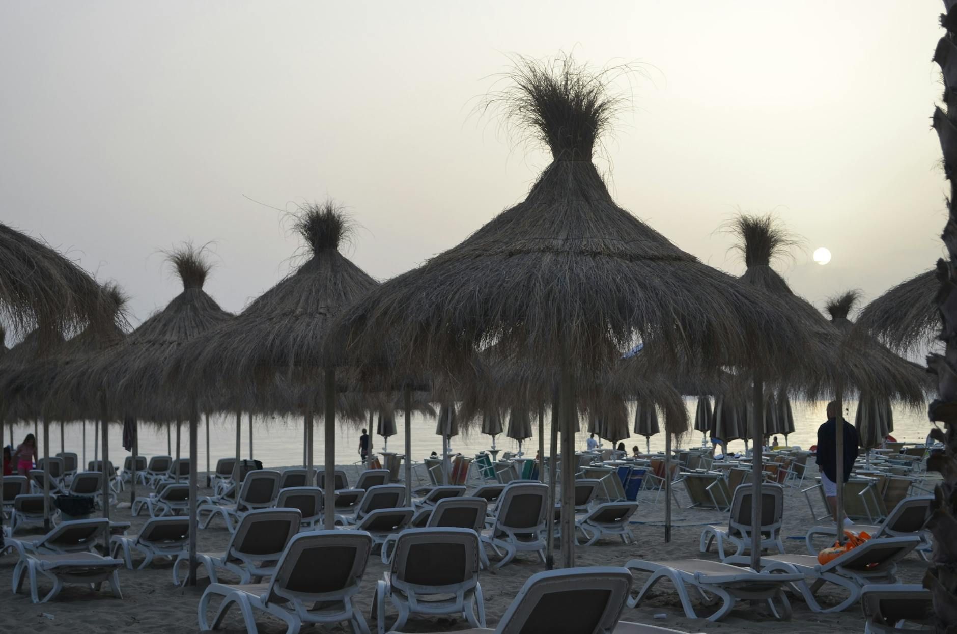 Tranquil beach setting in Durrës with straw umbrellas and chairs at sunset, ideal for a summer getaway.