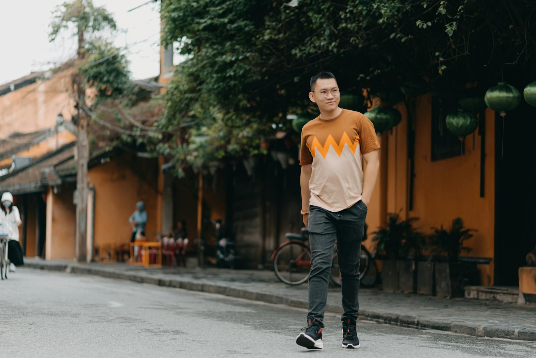 Full body of confident Asian man in casual wear walking on street at daytime while looking away and smiling