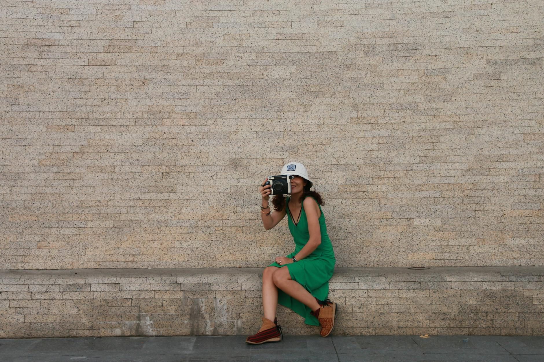 A woman with a camera sits against a vintage brick wall in Vietnam, capturing a timeless moment.