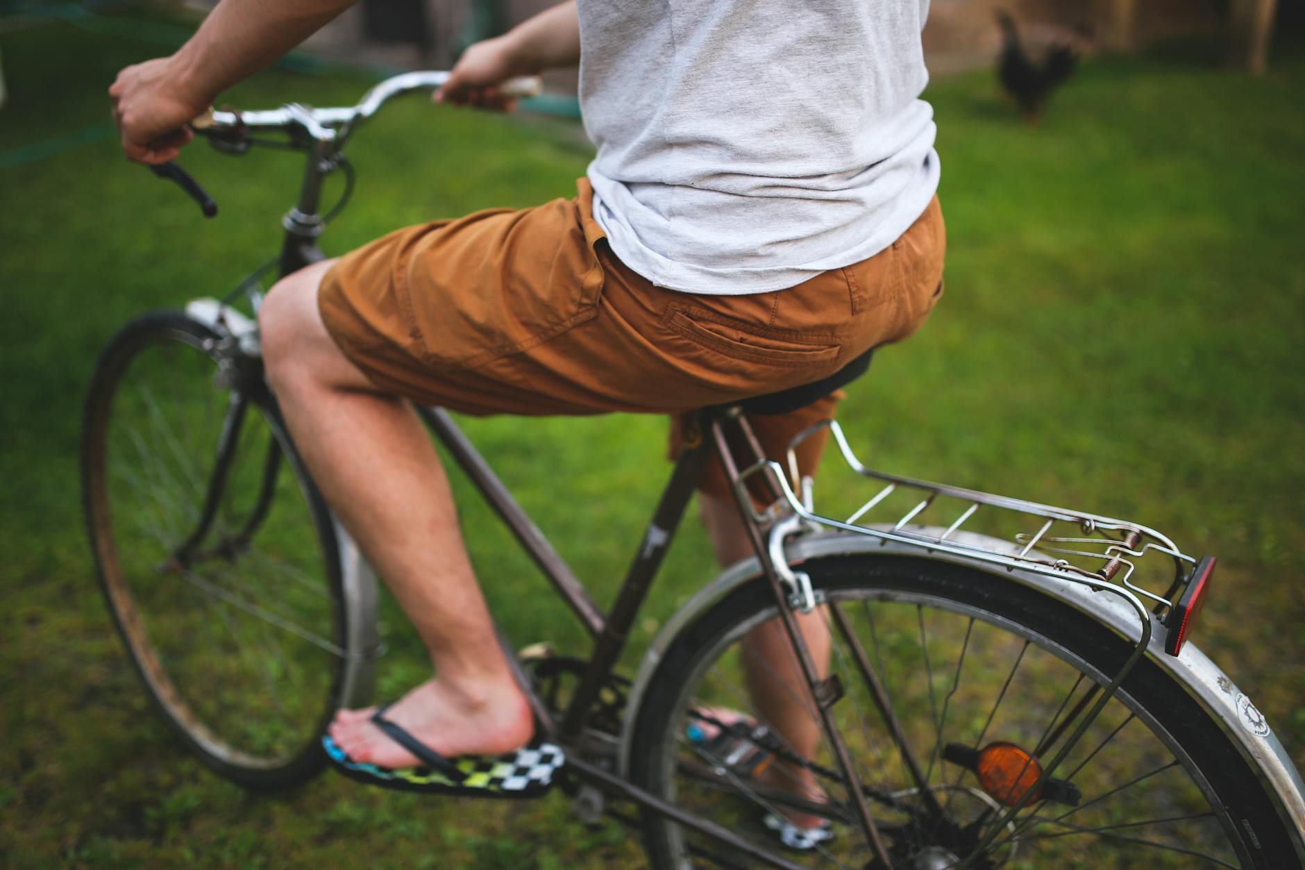 A person riding a bicycle in a park, wearing casual summer clothing and flip-flops.