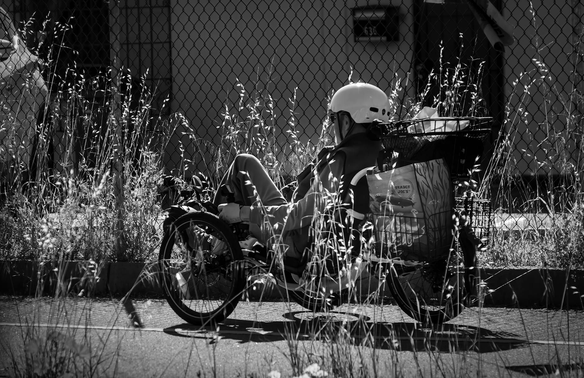 Black and white image of a cyclist riding a recumbent bike on a city street.