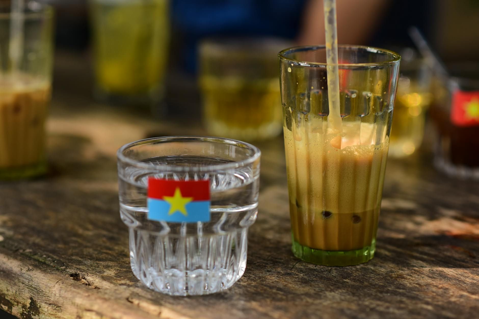 Close-up of Vietnamese iced coffee and water glass on a wooden table outdoors.