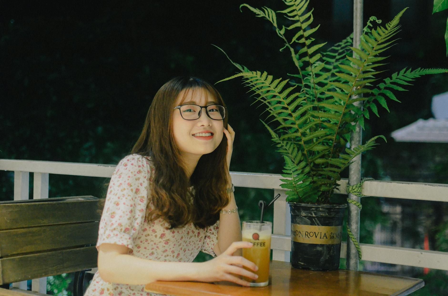 Young woman in glasses smiling with a beverage on a cozy outdoor terrace in Haiphong, Vietnam.