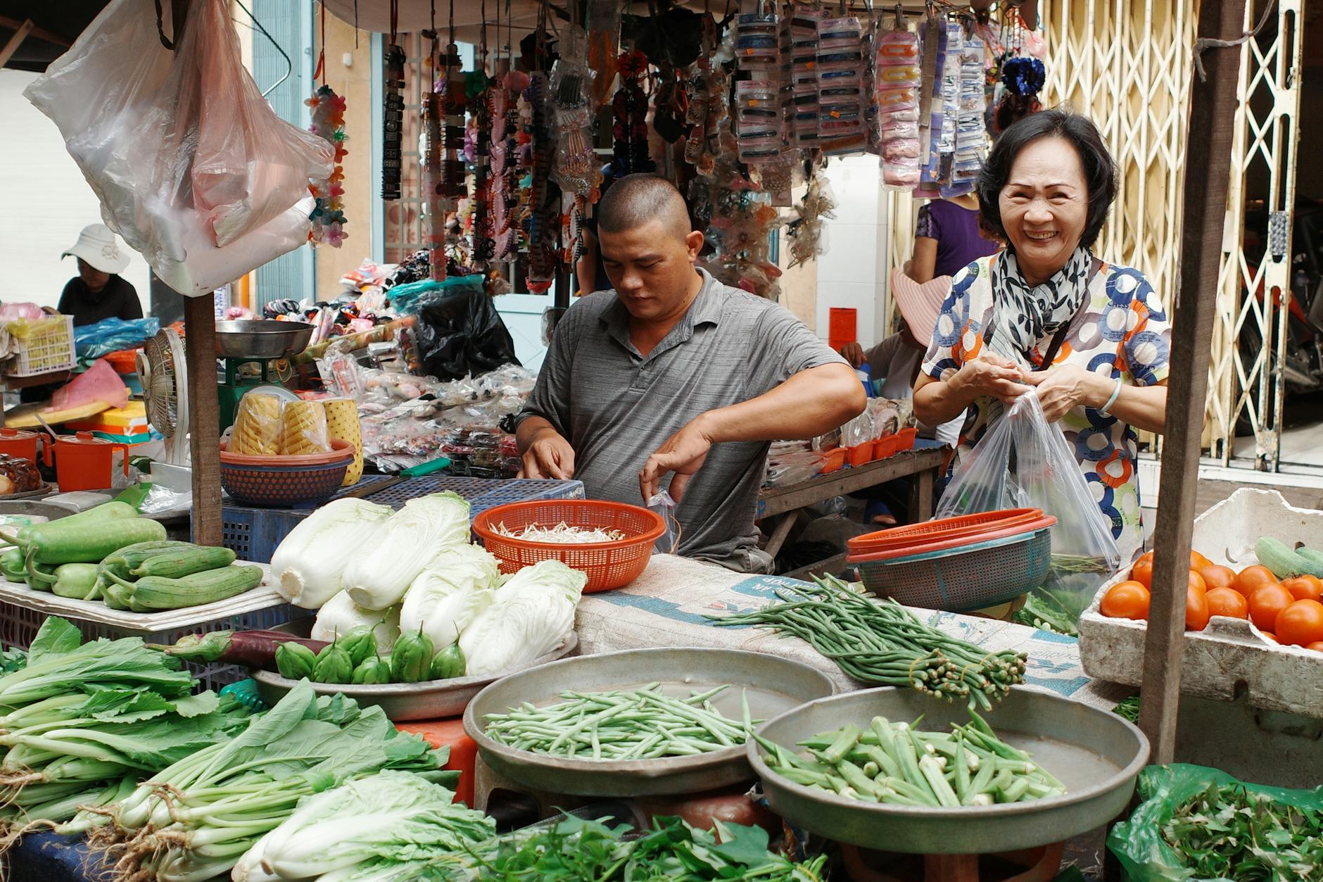 Smiling vendor and customer in a bustling Ho Chi Minh City street market with fresh produce.