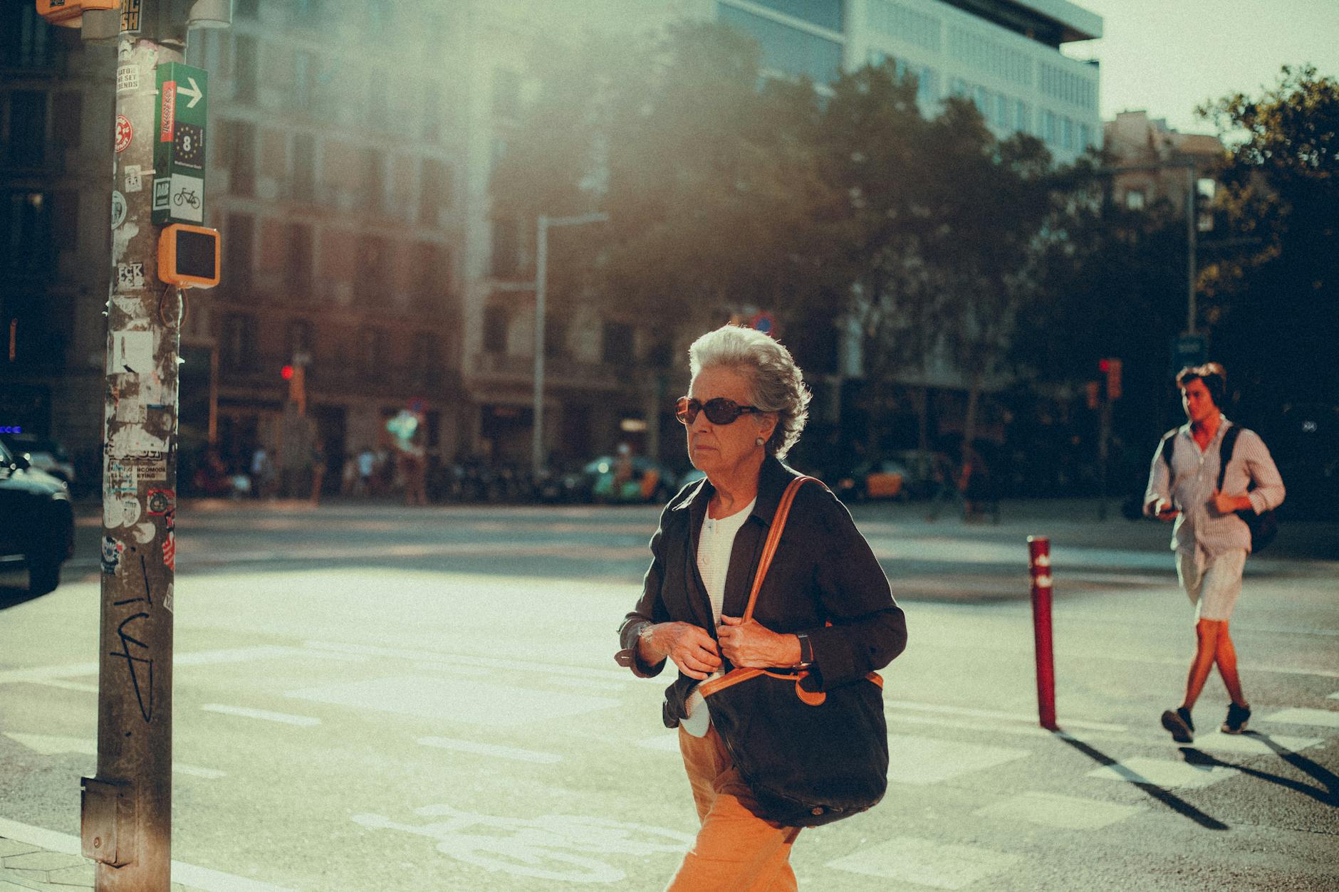 A senior woman with gray hair walks in a sunlit urban environment, embodying city life.