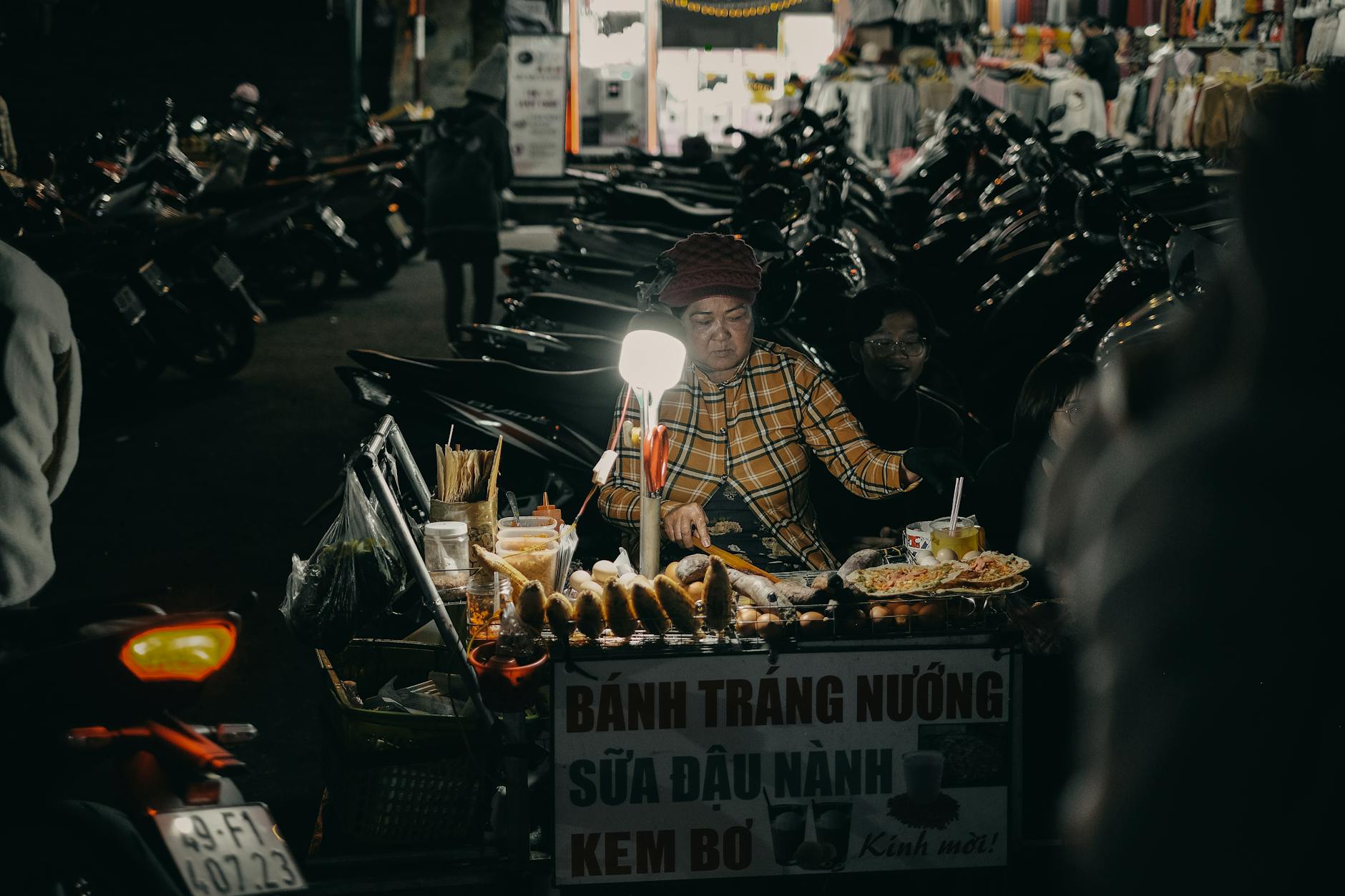 A busy street food vendor at night in a vibrant marketplace, surrounded by motorcycles.